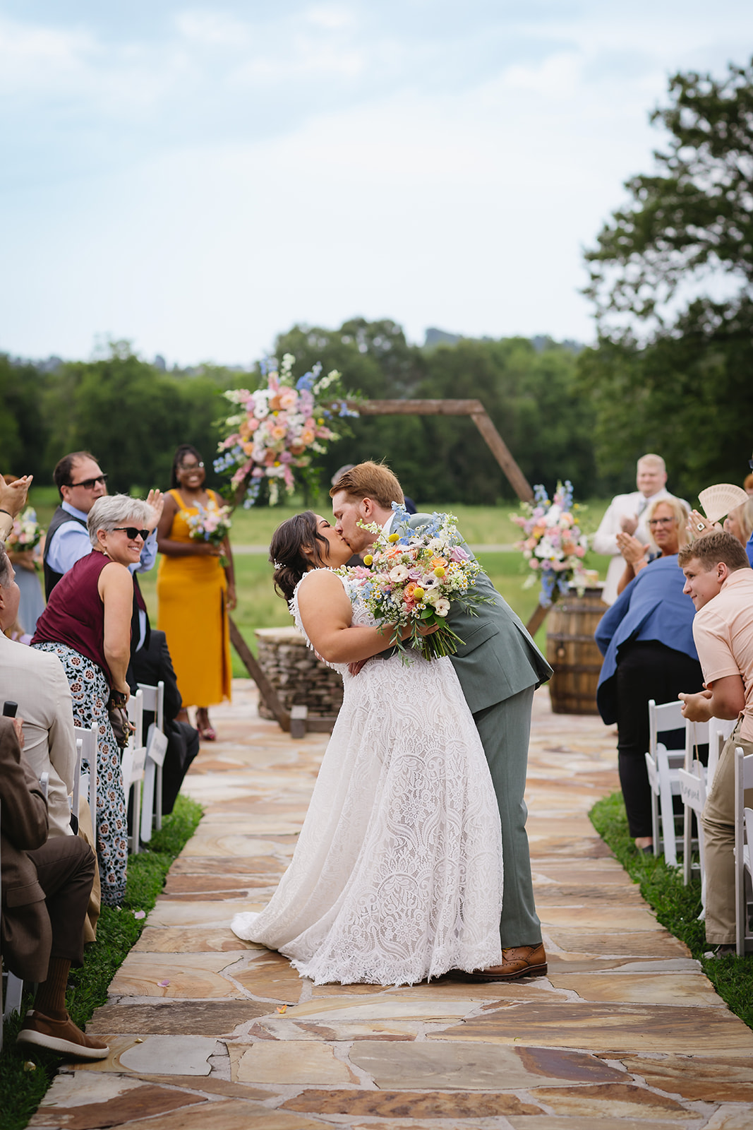 Meredith & Benjamin kiss at the aisle end as guests cheer by the Patio arch at Covey Creek