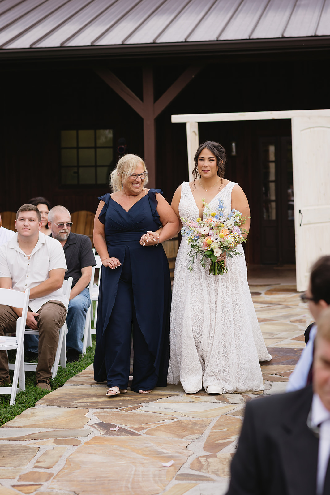 Meredith walks the stone aisle with her mother toward the barn for Meredith & Benjamin at Covey Creek