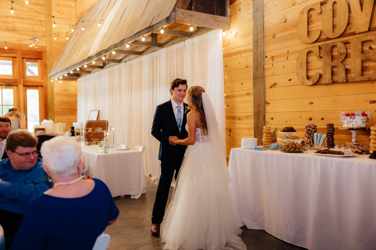 Morgan & Caden stand hand-in-hand by the dessert table and Covey Creek wall letters at indoor reception