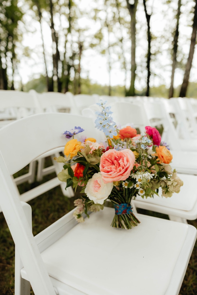 Morgan & Caden’s colorful bridal bouquet rests on a white chair at Covey Creek’s outdoor ceremony lawn