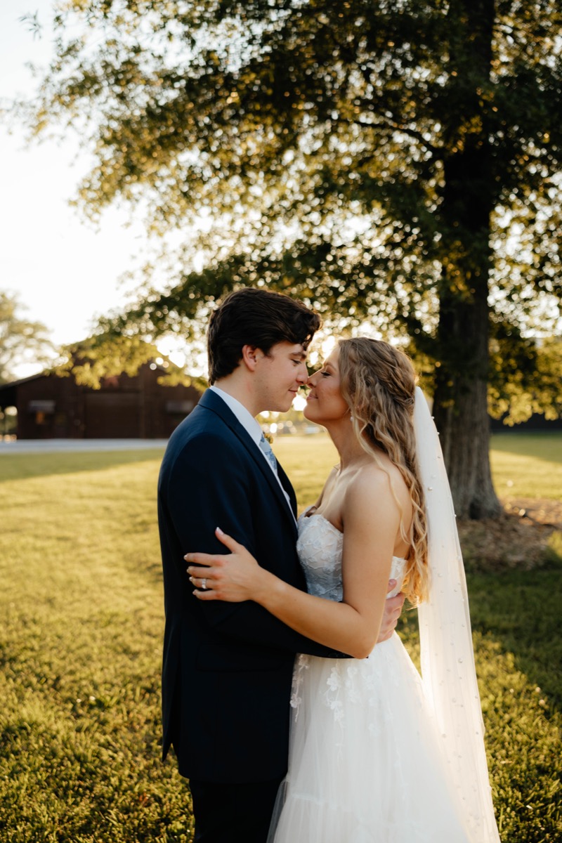 Morgan & Caden lean forehead-to-forehead at golden hour by Covey Creek’s barn, her pearl veil glowing