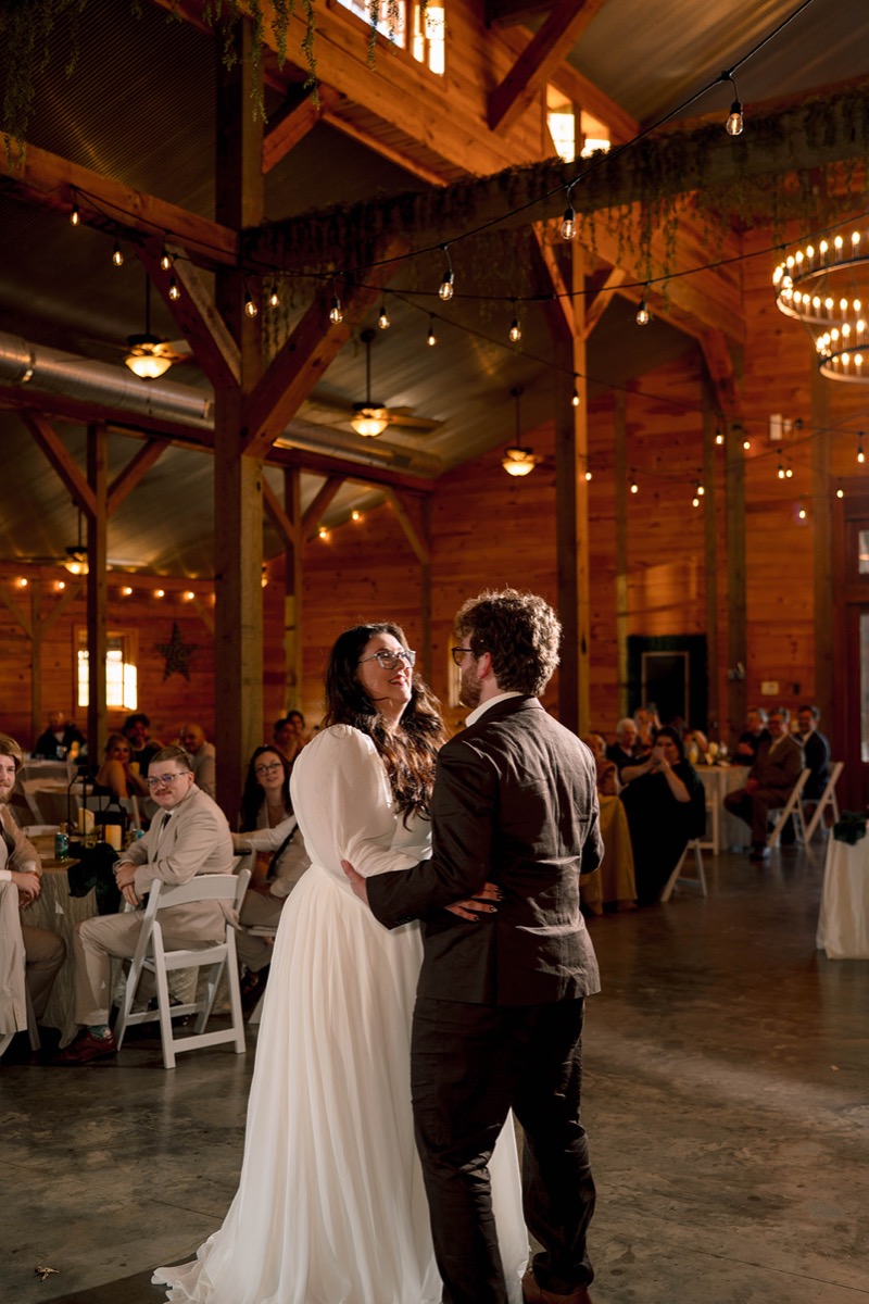 Peyton & Jackson share a first dance in the wood-paneled barn at Covey Creek under glowing string lights.