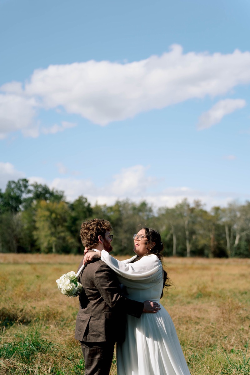 Peyton & Jackson laugh embracing in a golden grassy field under a bright blue sky at Covey Creek.