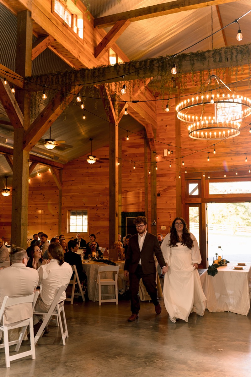Peyton & Jackson enter their reception under string lights and a wagon-wheel chandelier in Covey Creek's barn.