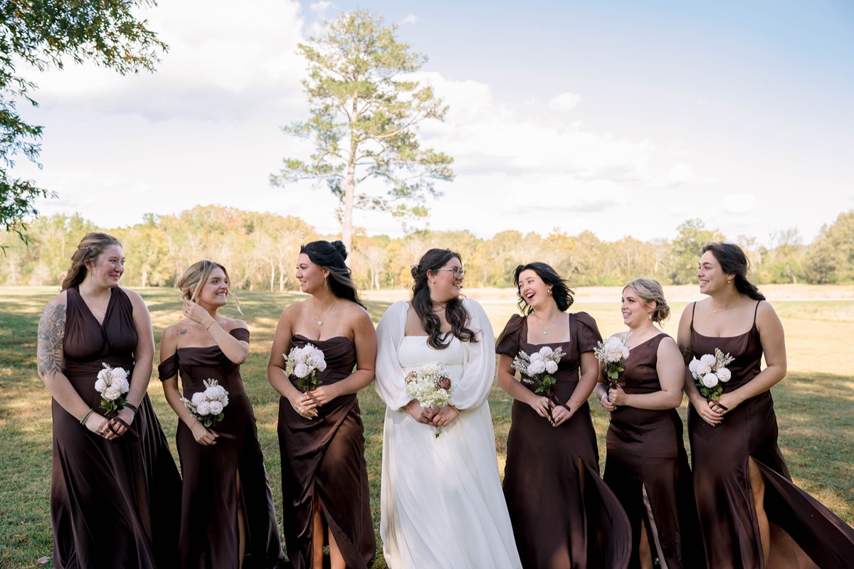 Peyton laughs with bridesmaids in chocolate dresses in a field at Peyton & Jackson's Covey Creek wedding.