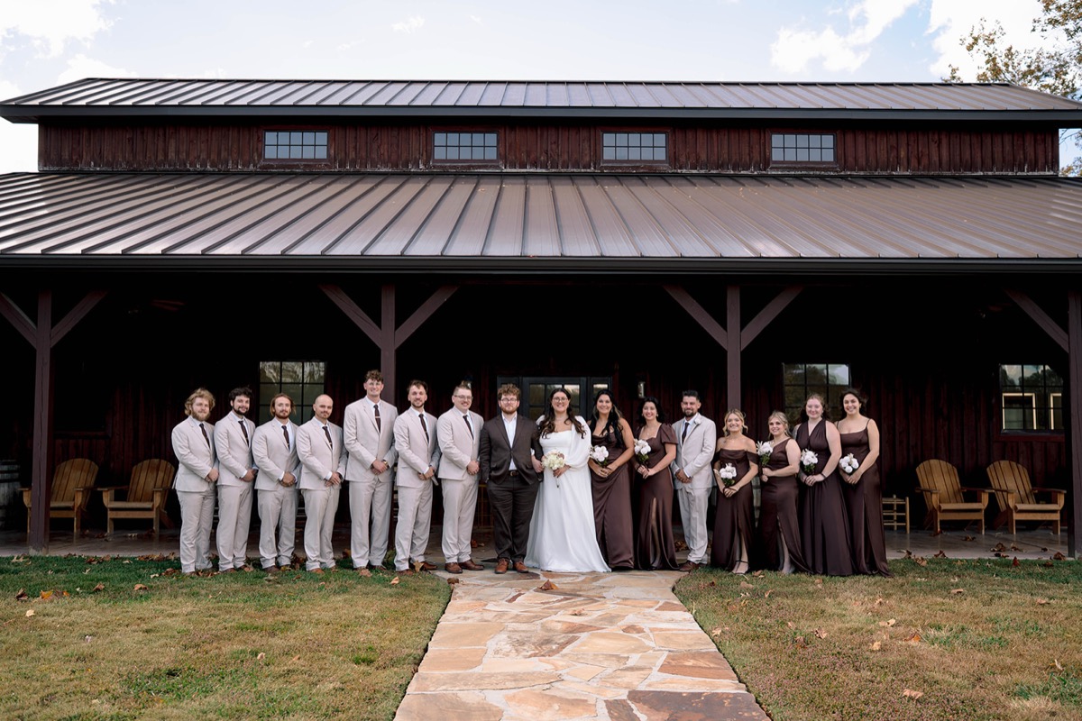 Peyton & Jackson pose with their wedding party before the rustic barn at Covey Creek on a sunny day.