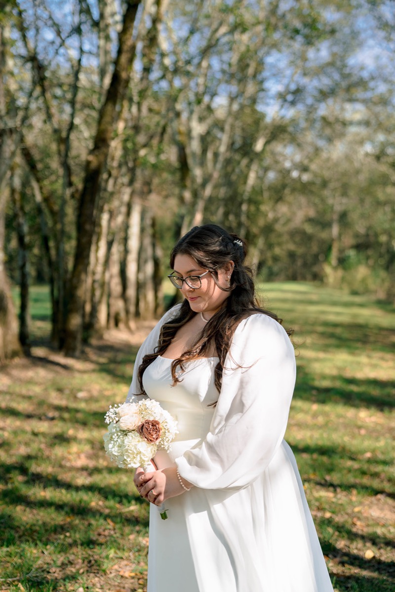 Peyton holds her white hydrangea bouquet among tall trees at Peyton & Jackson's Covey Creek wedding.