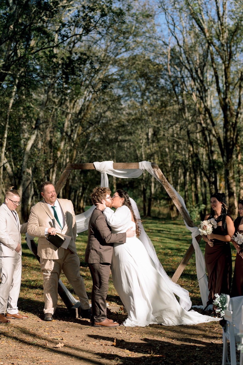 Peyton & Jackson share a first kiss under a white-draped hexagonal arbor in the woods at Covey Creek.