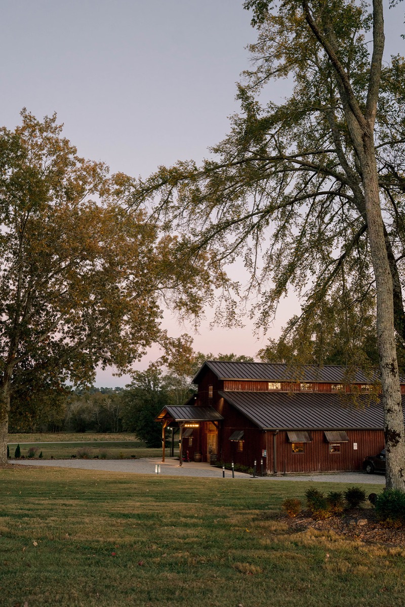 Covey Creek's wooden barn glows at dusk under a pink-purple sky for Peyton & Jackson's wedding day.