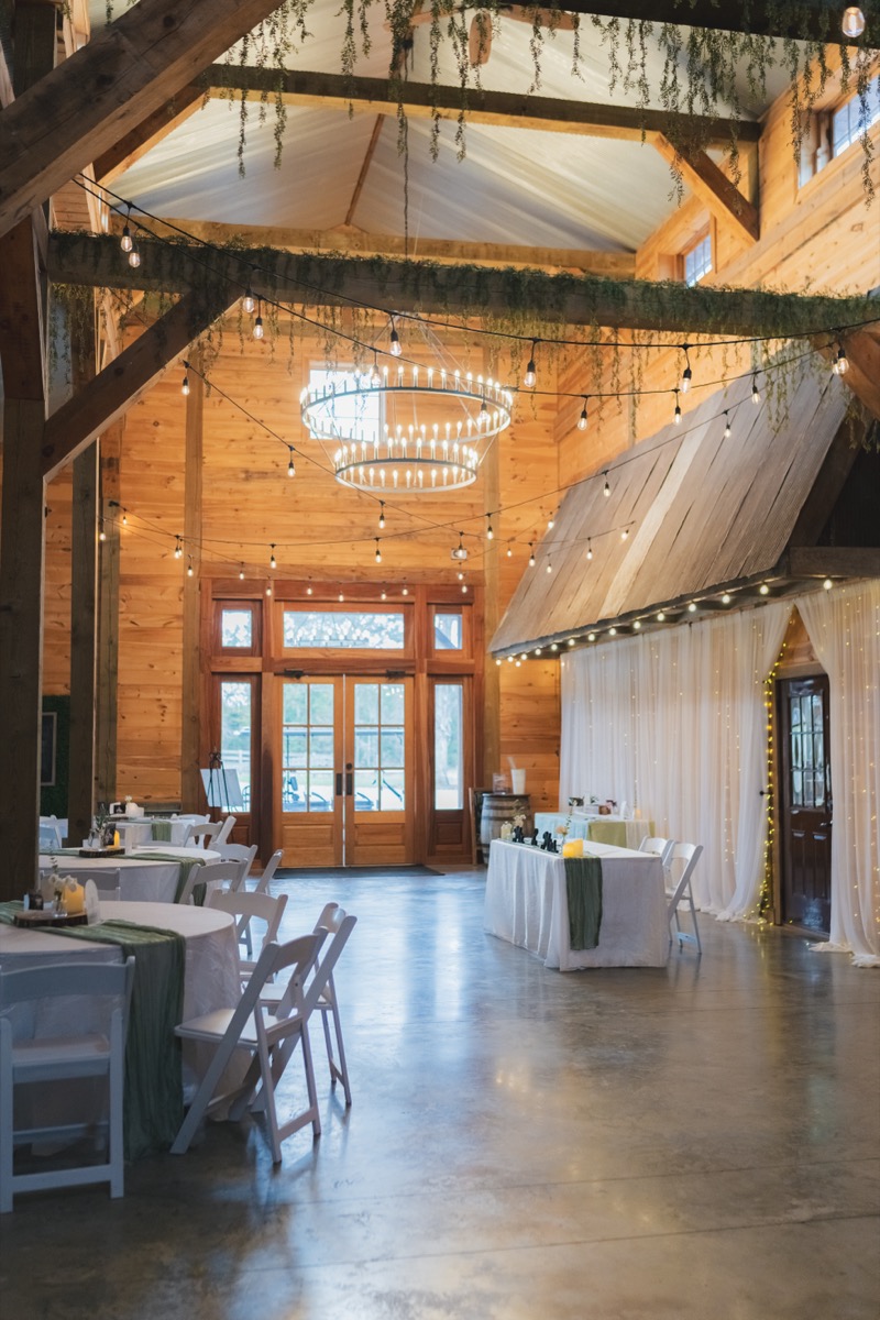 Rae & David indoor reception at Covey Creek with round tables, sage runners, chandelier, and string lights