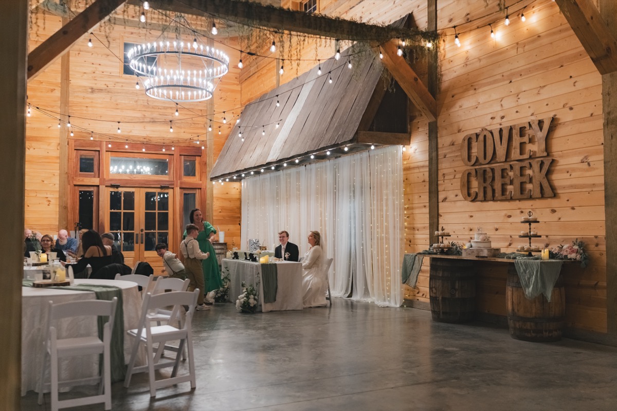 Rae & David sit at their sweetheart table near dessert barrels in the Covey Creek indoor reception