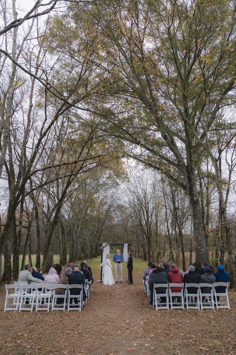 Guests face Rae & David under a floral arbor along the leaf-strewn Tunnel of Love aisle at Covey Creek