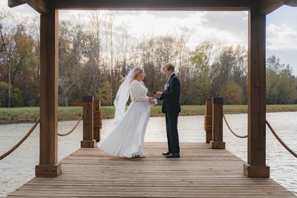 Rae & David exchange vows on the wooden dock at Covey Creek Pond, framed by pavilion timber beams