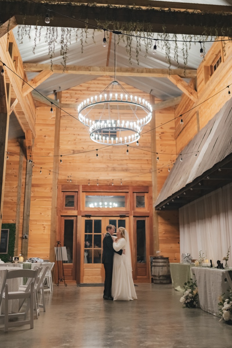 Rae & David first dance under a glowing chandelier in the Covey Creek indoor reception barn hall