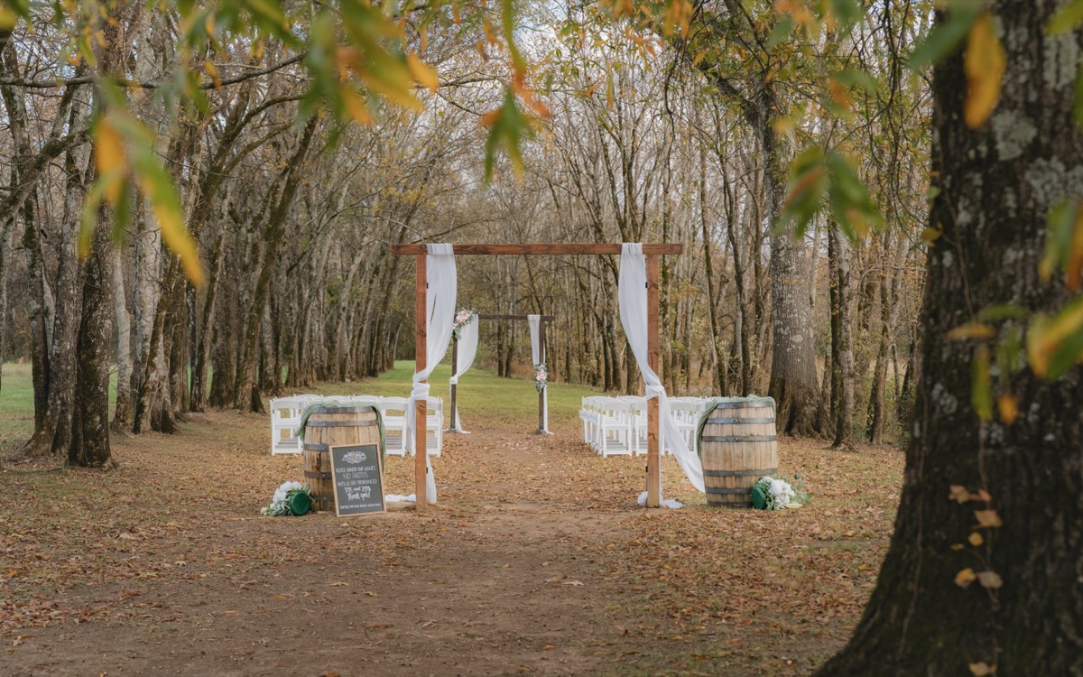 Tunnel of Love ceremony aisle for Rae & David at Covey Creek with wooden arbor, white chairs, and barrels