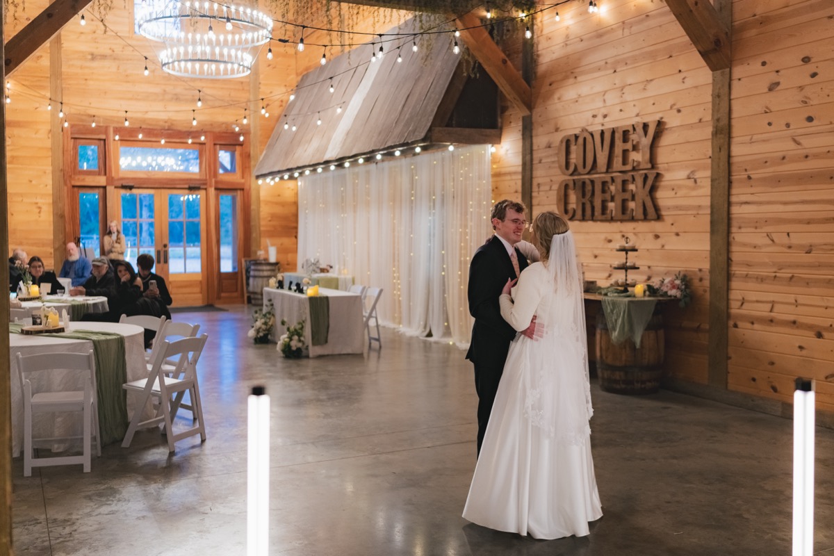 Rae & David dance during indoor reception at Covey Creek beside sage-dressed tables and wood lettering
