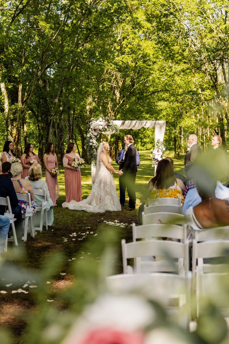 Raven & Jackson hold hands under a floral wooden arbor during their outdoor ceremony at Covey Creek