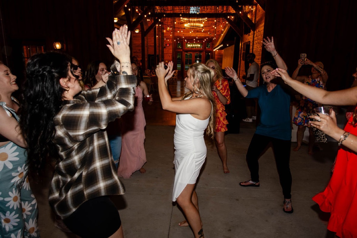 Raven dances with guests in a short white dress under string lights at Covey Creek for Raven & Jackson