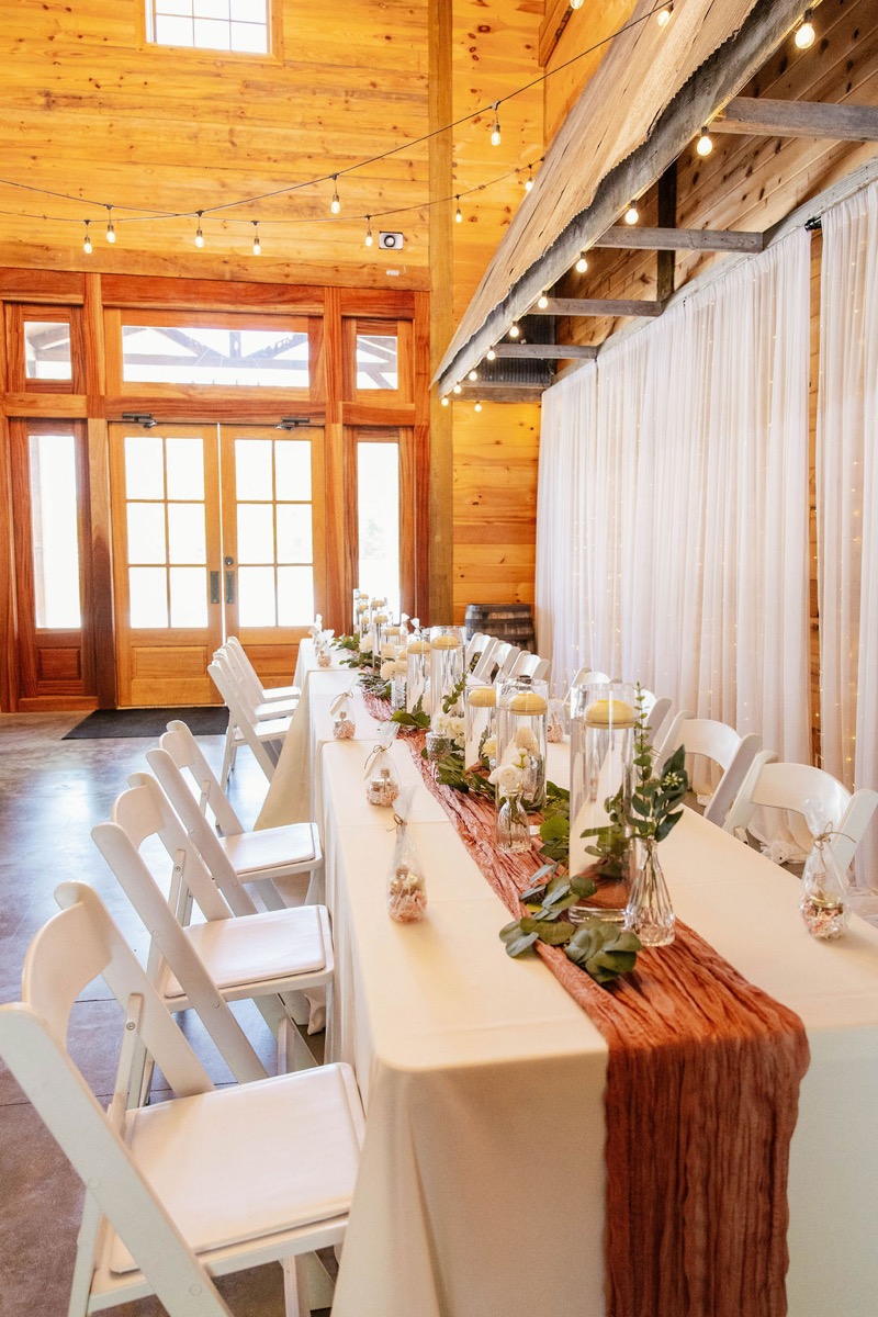 Long head table for Raven & Jackson at Covey Creek with terracotta runner, floating candles, greenery, and string lights