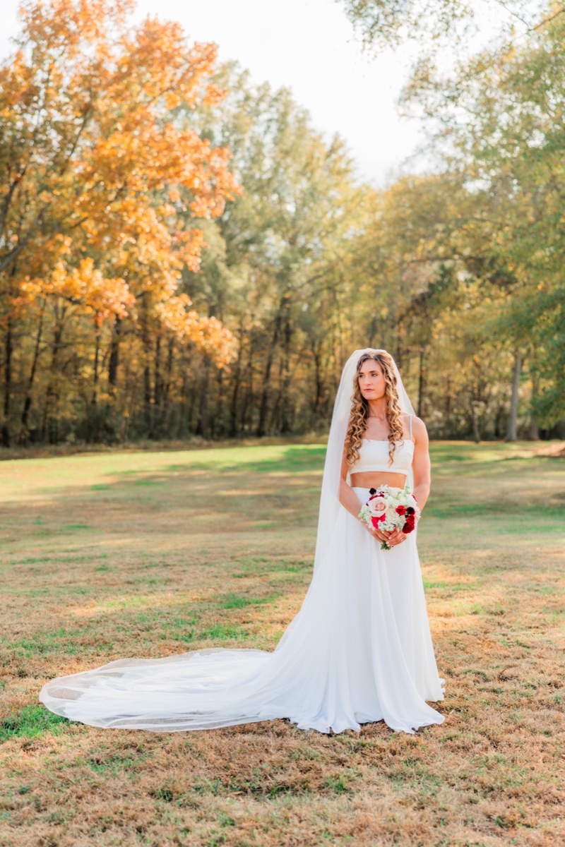 Sarah & Adam's bride stands veiled in a grassy field holding a red rose bouquet at Covey Creek