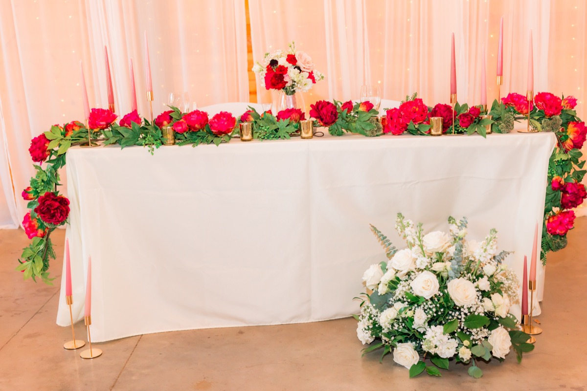 Sarah & Adam's sweetheart table with red floral garland and pink taper candles at Covey Creek