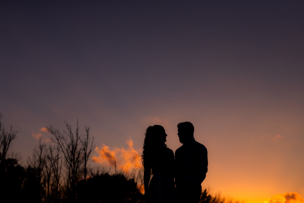 Silhouette of Sarah & Adam facing each other against a vivid orange sunset sky at Covey Creek