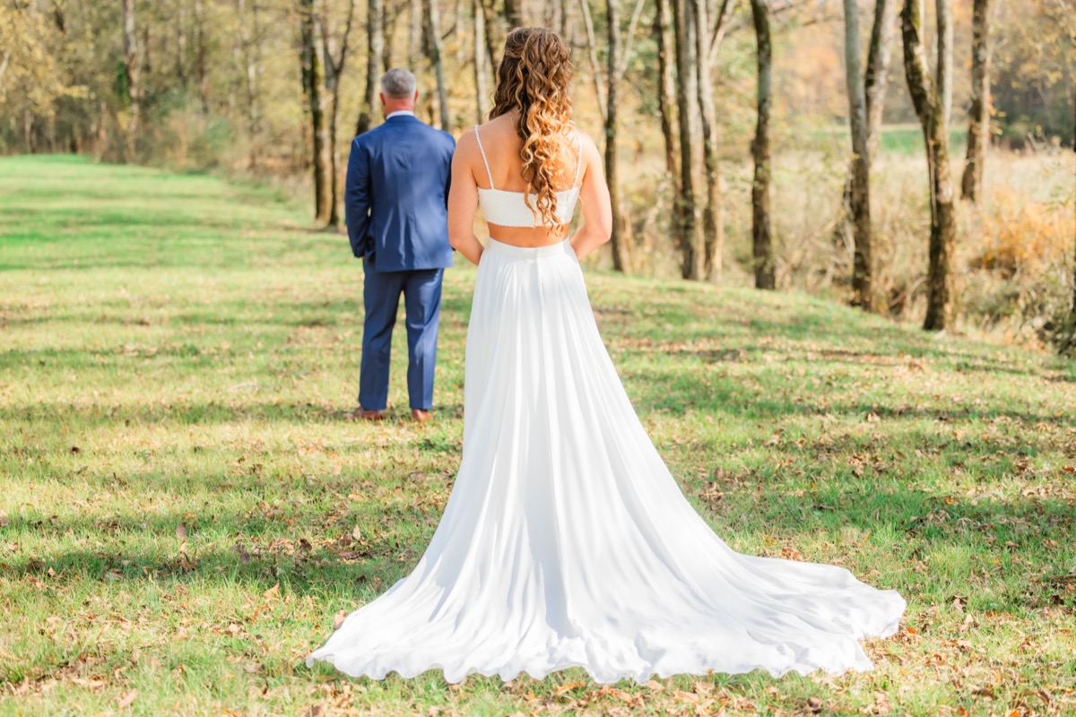 Sarah & Adam share a first-look moment in a grassy autumn field as she approaches him at Covey Creek