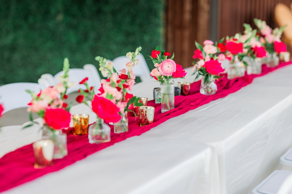 Long reception table with red runner, pink florals, and white chairs for Sarah & Adam at Covey Creek