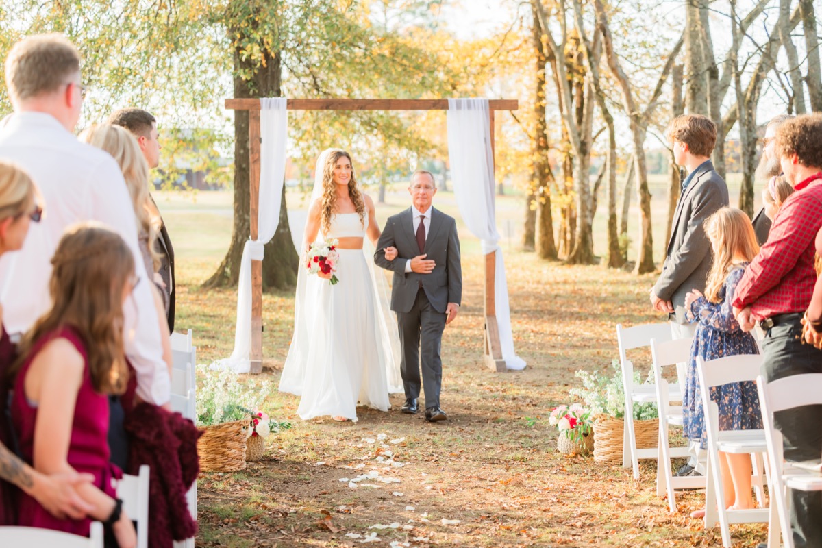 Sarah & Adam's bride walks the petal-strewn aisle with her father past guests at Covey Creek