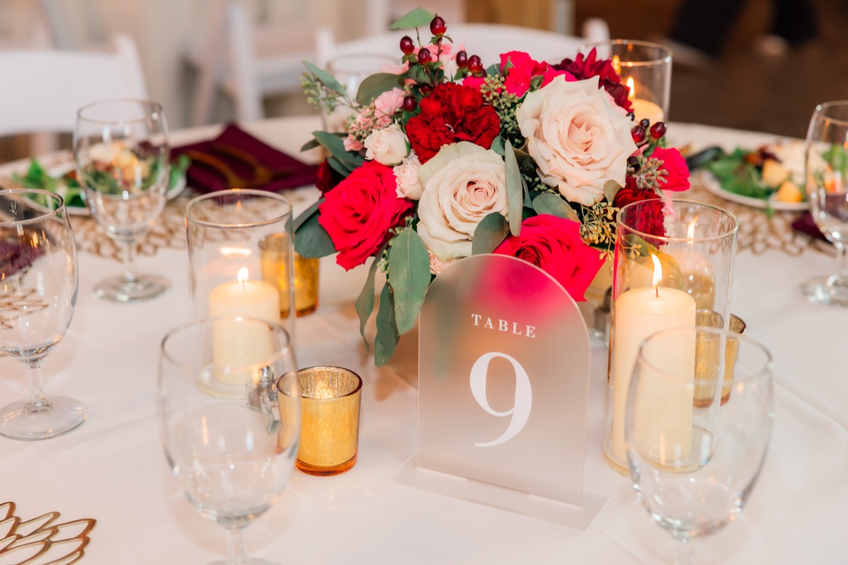 Acrylic table nine sign with red rose centerpiece and pillar candles at Sarah & Adam's Covey Creek reception