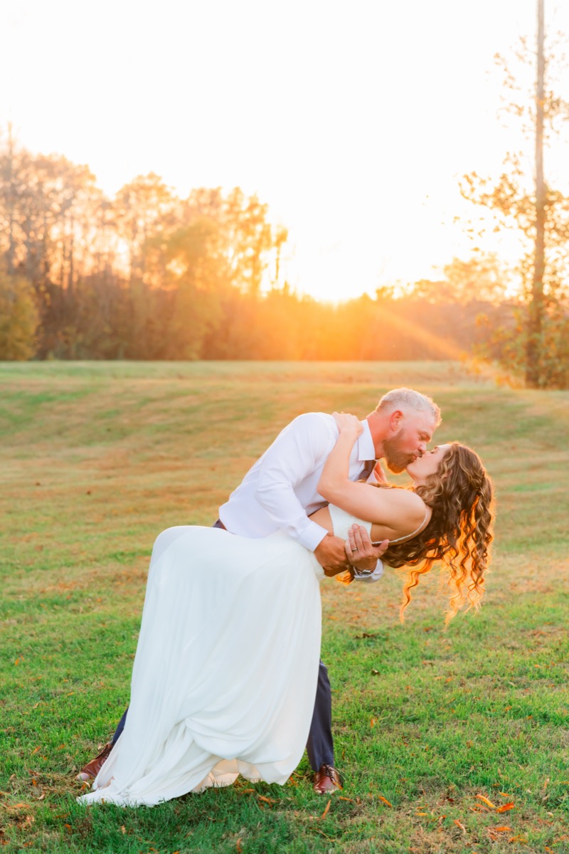 Sarah & Adam share a golden-hour dip kiss in an open grassy field at their Covey Creek wedding