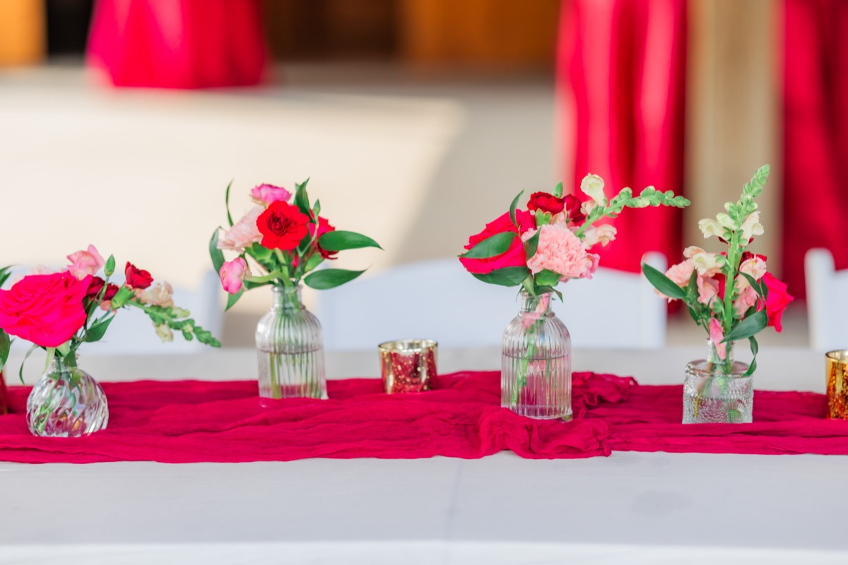 Crimson runner, bud vases of pink and red blooms, and gold votives at Sarah & Adam's Covey Creek reception