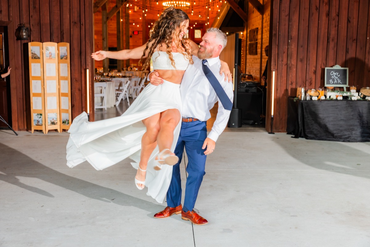 Sarah & Adam laugh as he lifts her outside the open barn doors at their Covey Creek wedding