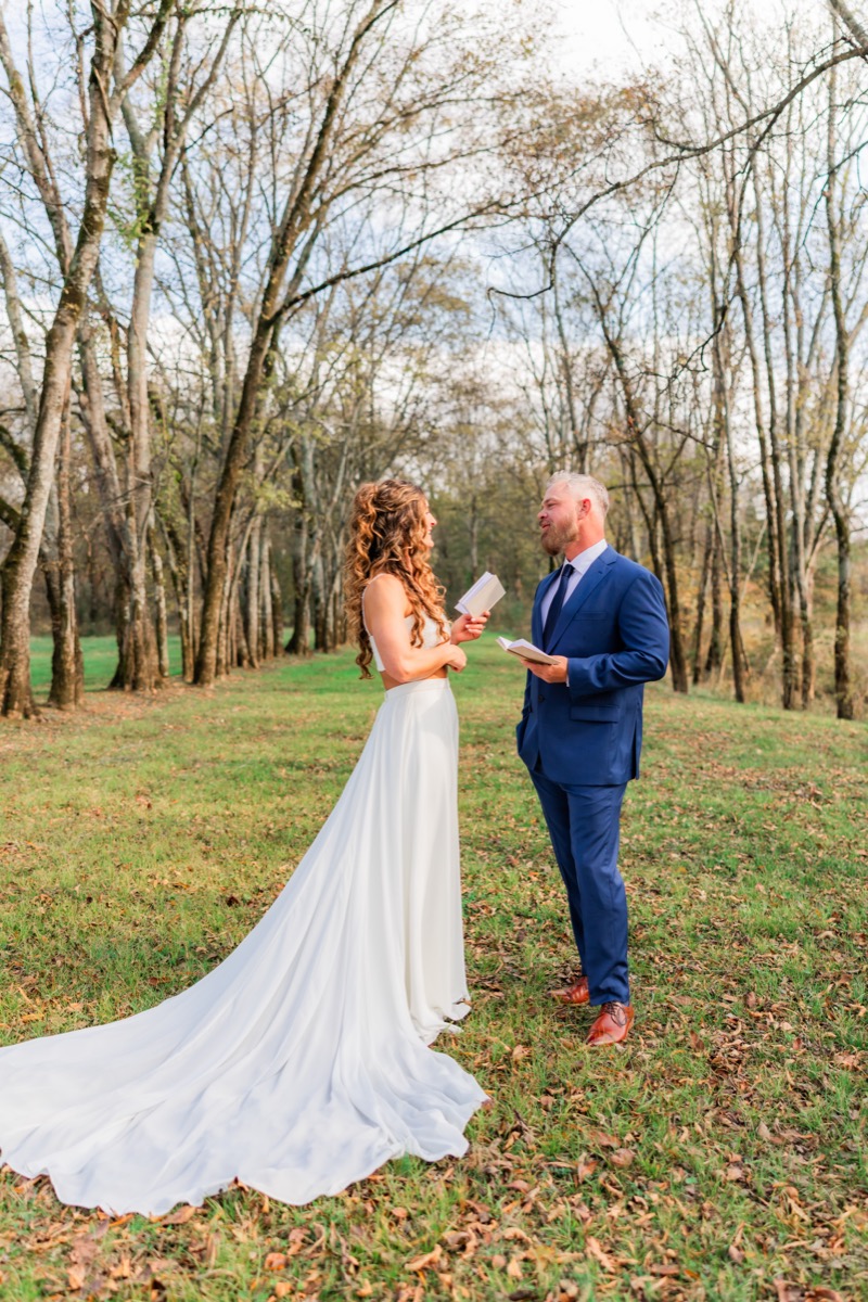 Sarah & Adam read private vows from white booklets in a leaf-strewn autumn field at Covey Creek