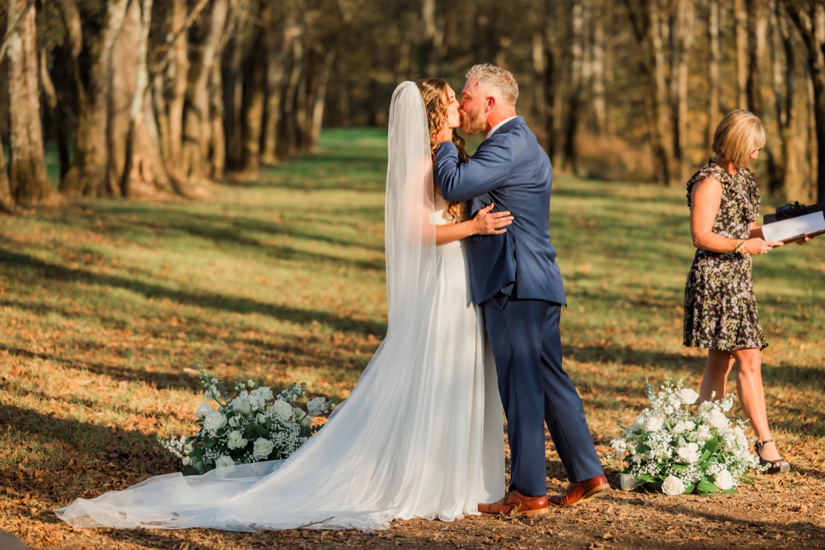 Sarah & Adam share their first kiss beside white floral arrangements at their Covey Creek ceremony