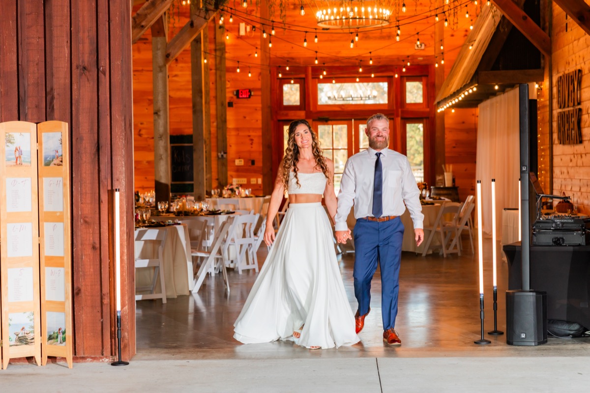 Sarah & Adam enter the string-lit barn reception hand-in-hand on their Covey Creek wedding day