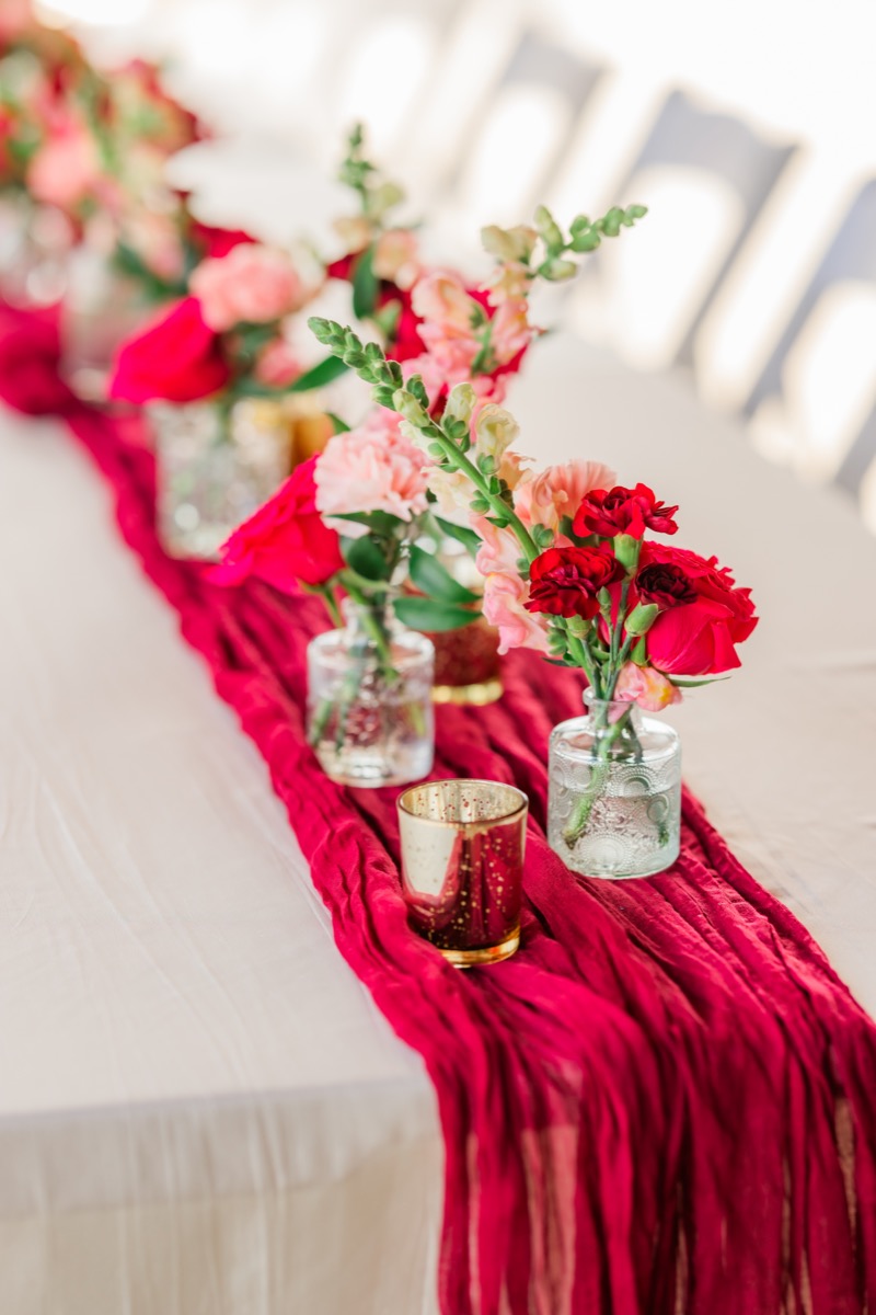 Red gauze runner with pink and red floral bud vases on Sarah & Adam's Covey Creek reception table