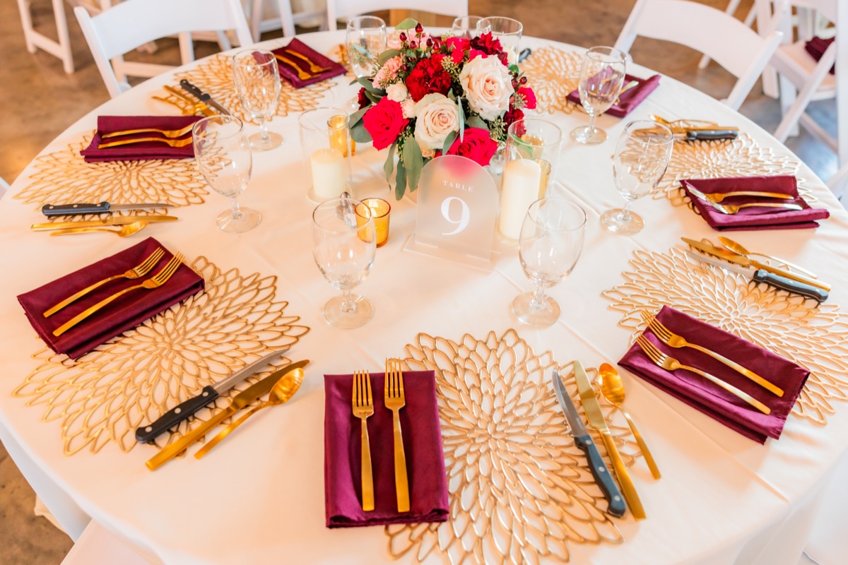 Table nine with red rose centerpiece, gold placemats, and burgundy napkins at Sarah & Adam's Covey Creek reception
