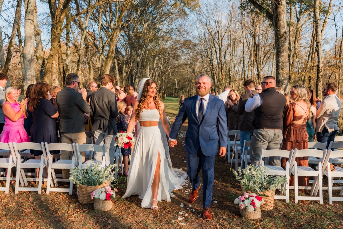 Sarah & Adam recess down the petal aisle as guests cheer at their Covey Creek outdoor ceremony