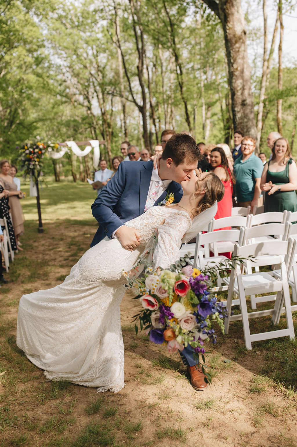 Jacob dips Shay for a kiss on the aisle at Covey Creek, colorful bouquet hanging as guests cheer behind them.