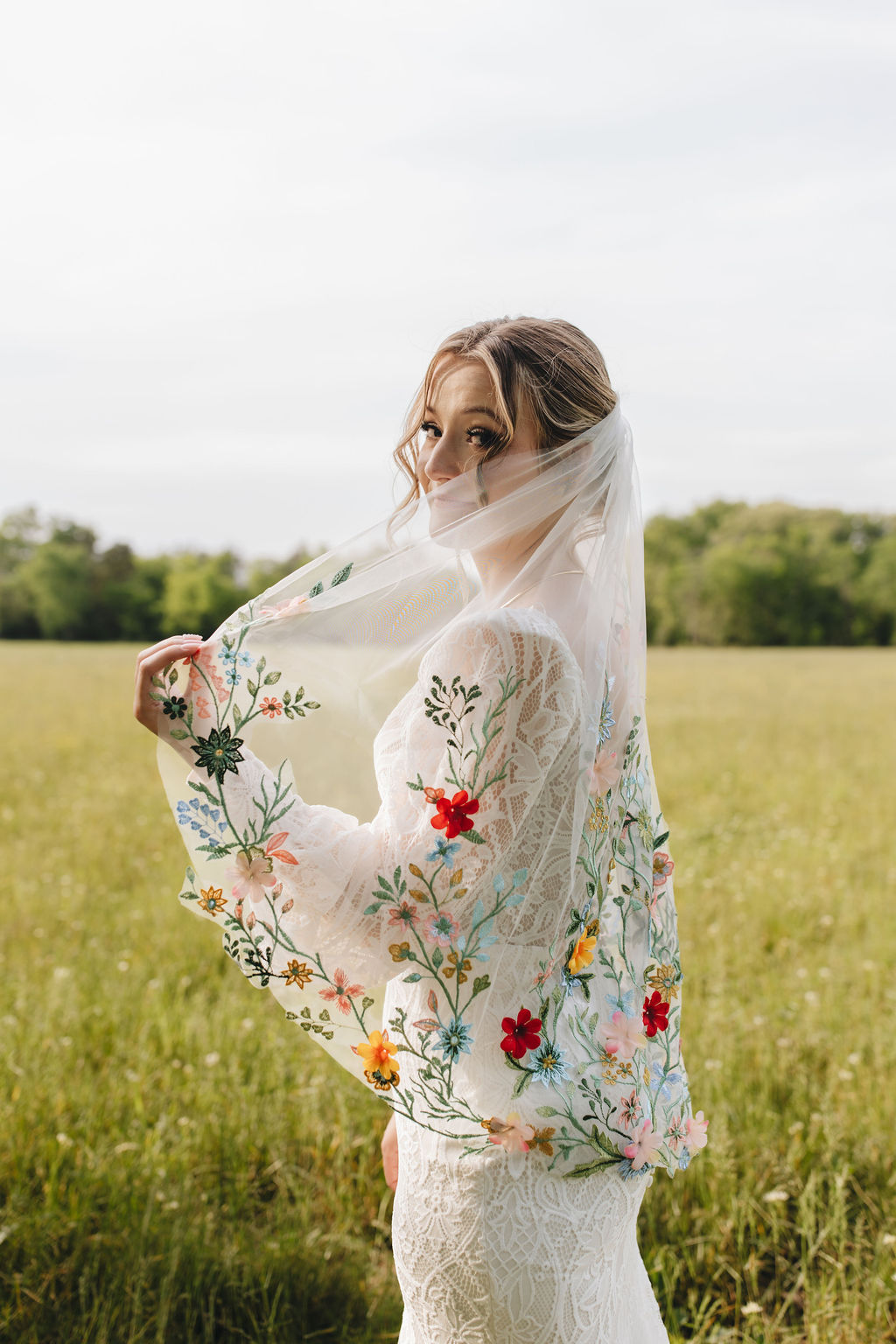 Shay looks back over her shoulder, lifting her colorful embroidered veil against Covey Creek’s open green field.