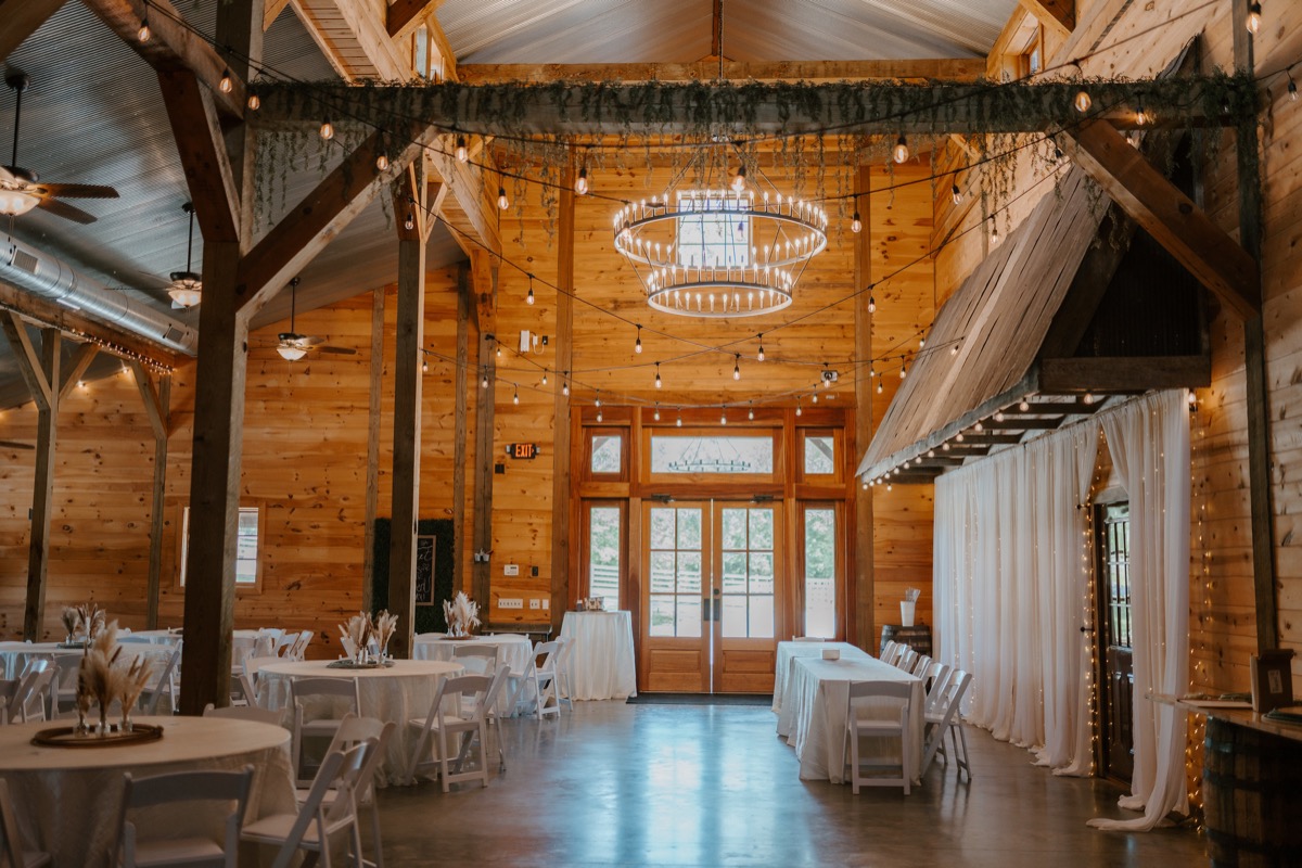 Shay & Wyatt's Covey Creek reception barn with white tables, string lights, and a glowing circular chandelier.