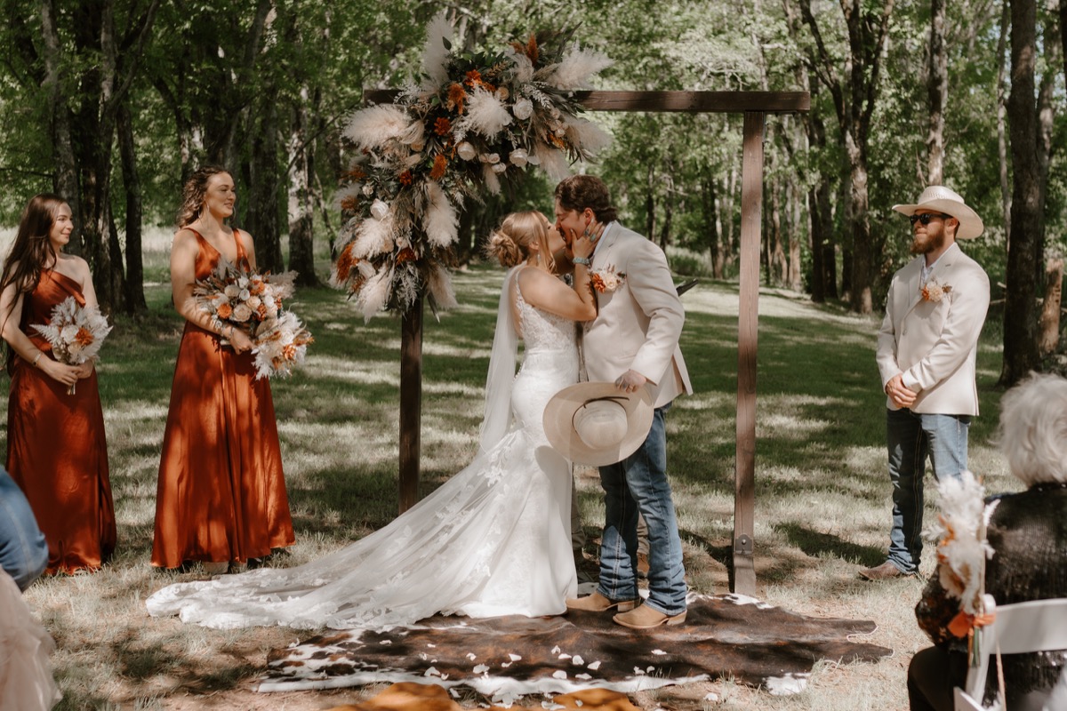 Shay & Wyatt share a first kiss under a pampas-and-orange floral arbor on a cowhide rug at Covey Creek.