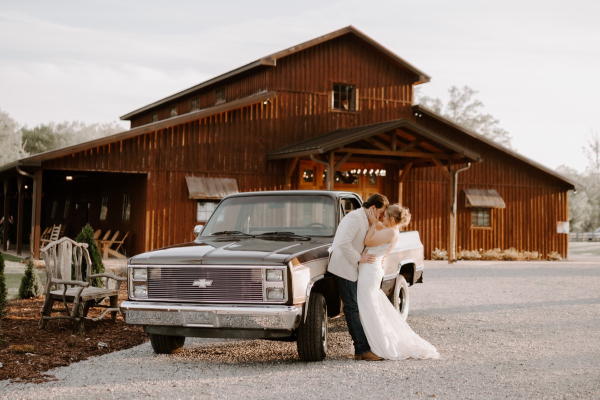 Shay & Wyatt kiss beside a vintage Chevy pickup on the gravel drive before the barn at Covey Creek.