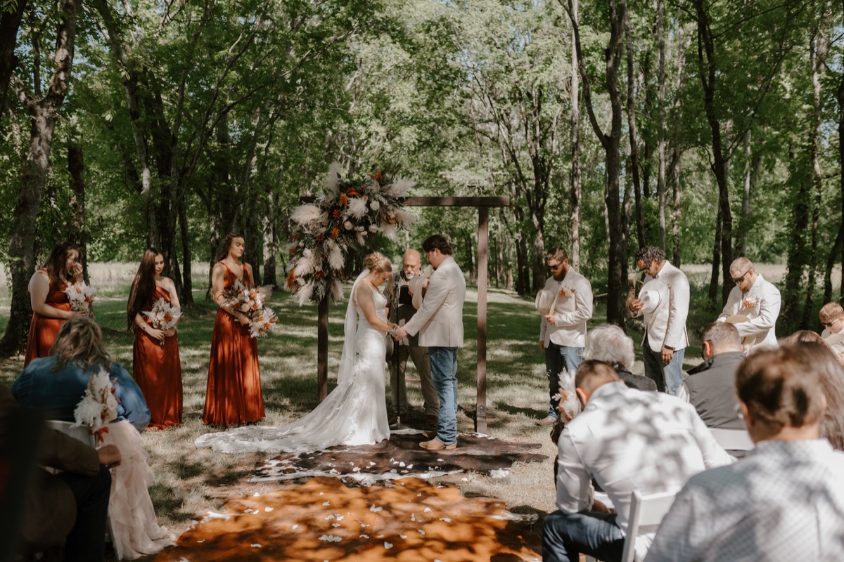 Shay & Wyatt stand at the altar under a floral arbor as guests watch their wooded ceremony at Covey Creek.