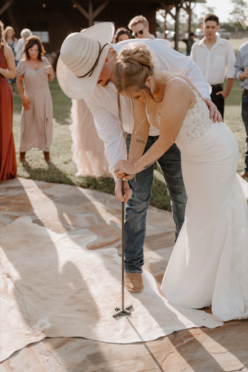 Shay & Wyatt press a branding iron into a cowhide rug on the patio during their ceremony at Covey Creek.