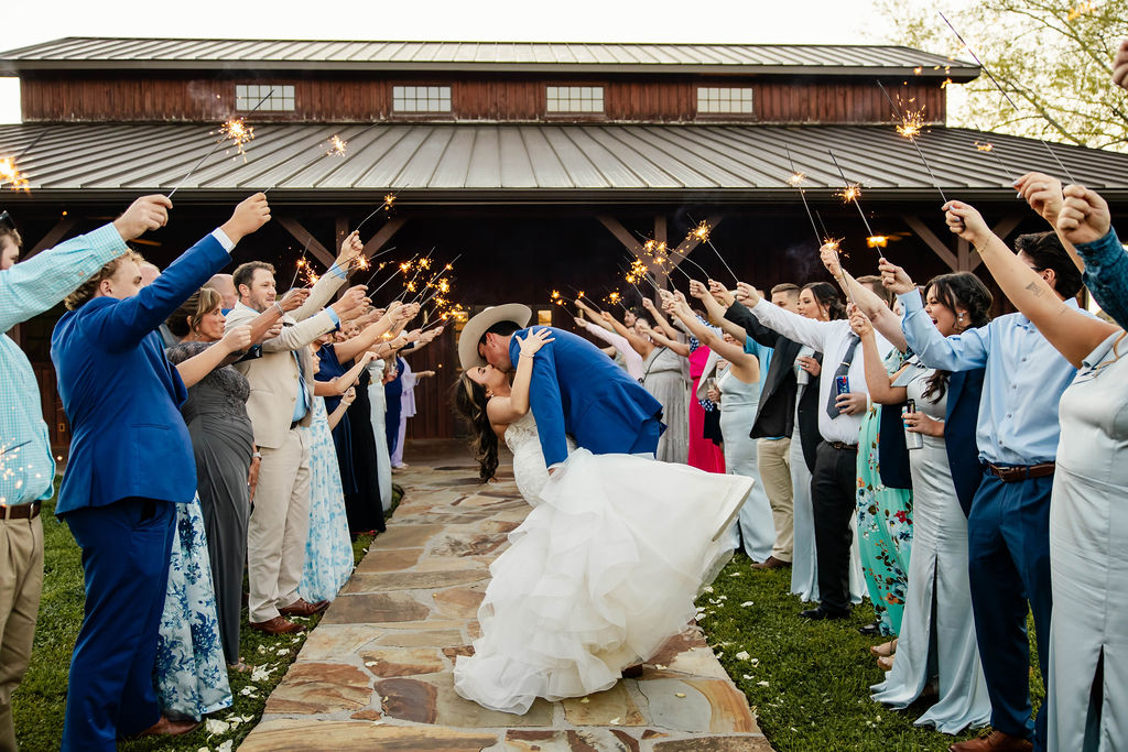 Shelbie & Callaway kiss in a dip during a sparkler exit on the stone path by the barn at Covey Creek