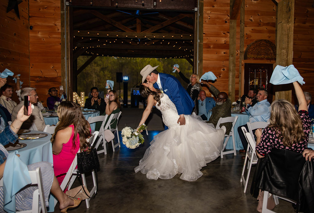 Shelbie & Callaway dip kiss on the barn dance floor as guests wave blue napkins at Covey Creek reception