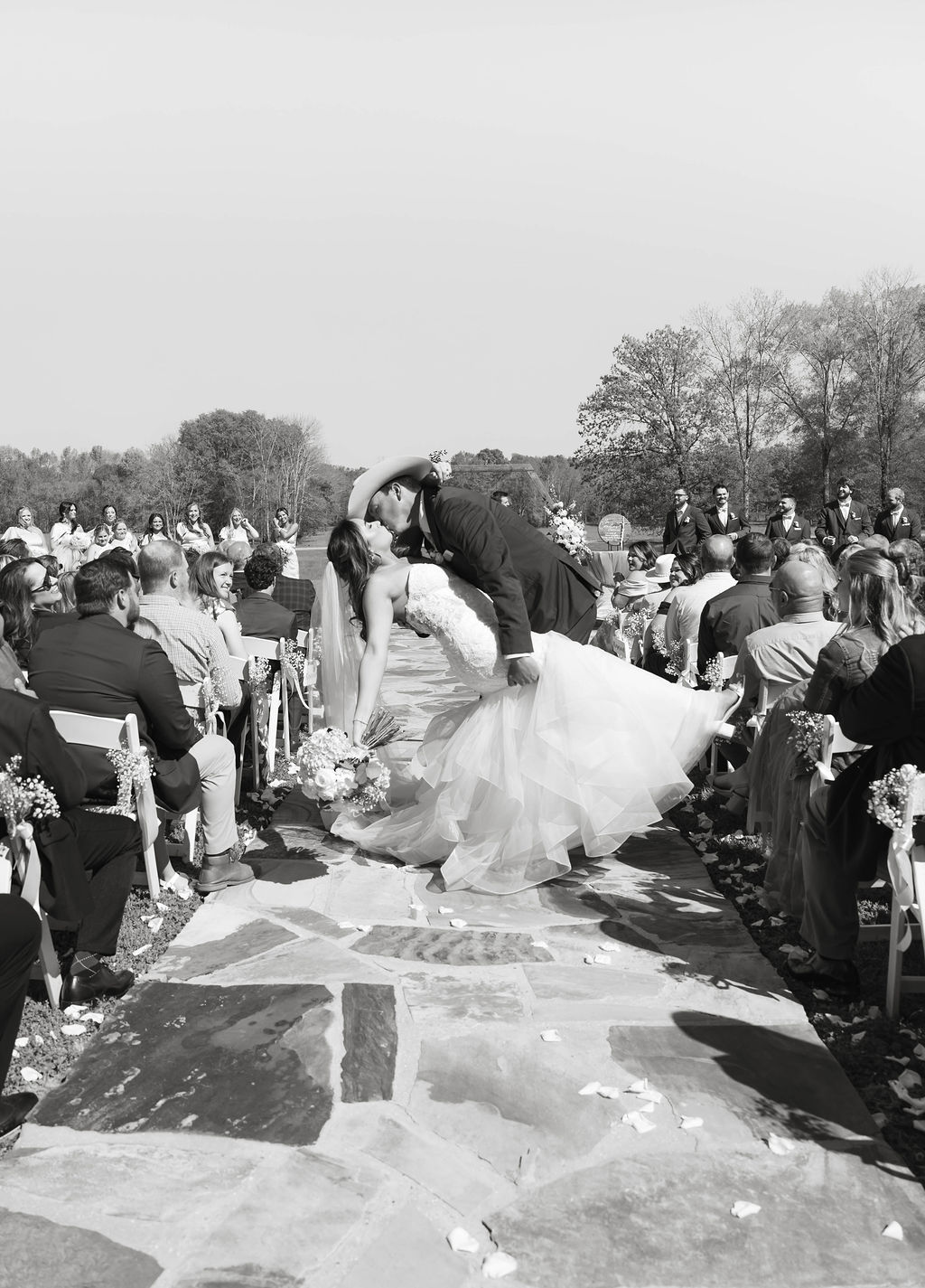 Shelbie & Callaway black-and-white dip kiss on the Firepit stone aisle with guests seated at Covey Creek