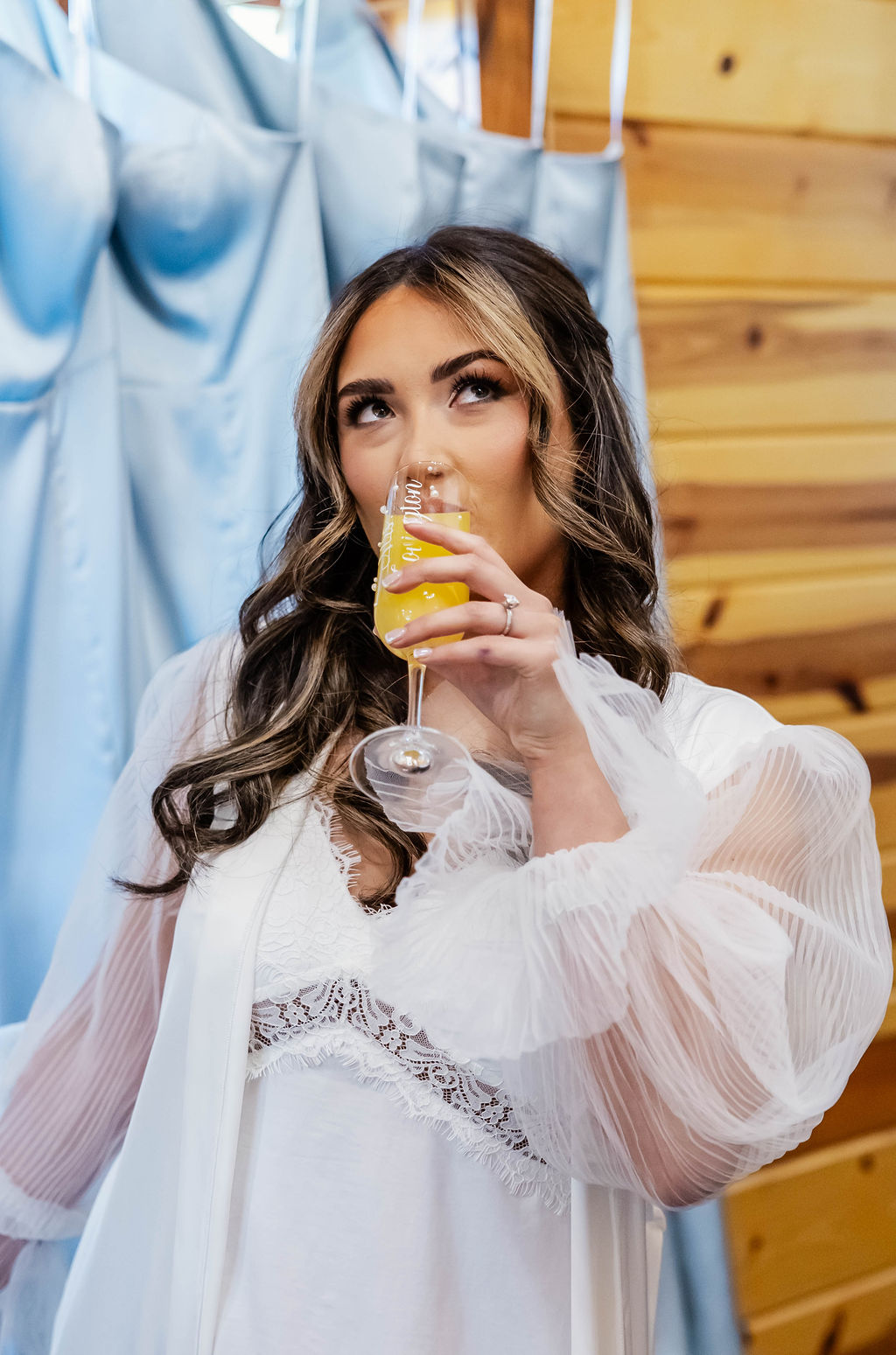 Shelbie & Callaway: Shelbie in a lace robe sips champagne beside hanging blue bridesmaid dresses at Covey Creek